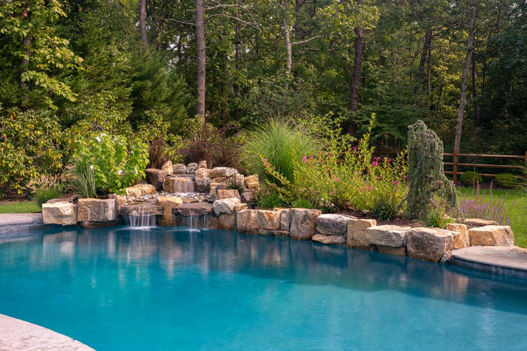 Natural stone boulder waterfall cascading into a pool surrounded by lush garden greenery