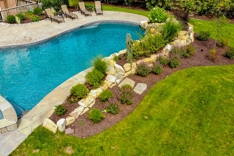 Natural stone boulder waterfall cascading into a pool surrounded by lush garden plants