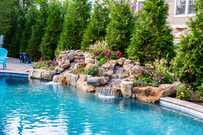 Joren C - Long Beach Island, NJ - A swimming pool with a waterfall feature surrounded by lush greenery and colorful flowers