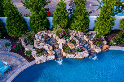 Joren D - Long Beach Island, NJ - A swimming pool surrounded by lush greenery and colorful flowers, with a waterfall feature