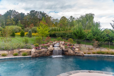 Juba B - Flemington, NJ - A swimming pool with a waterfall surrounded by lush greenery and colorful flowers
