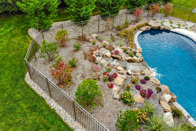 Natural stone boulder waterfall cascading into a pool surrounded by colorful shrubs and flowers