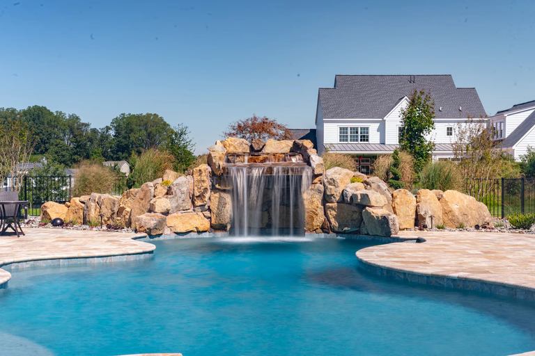 Natural stone boulder waterfall cascading into a freeform pool with surrounding greenery