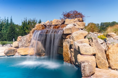 Kamui D - Phoenix, MD - A large rock waterfall in the middle of a swimming pool surrounded by greenery