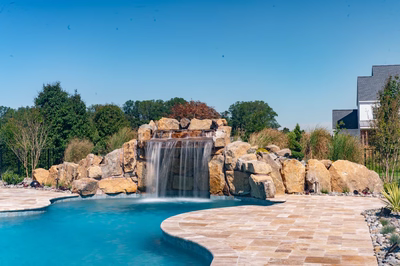 Kamui E - Phoenix, MD - A large rock waterfall in the middle of a swimming pool surrounded by lush greenery