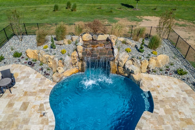 Kamui H - Phoenix, MD - A swimming pool with a waterfall in the middle surrounded by a stone patio and a black fence