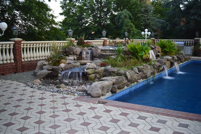 Kander D - Holmdel, NJ - A swimming pool surrounded by lush greenery and a stone waterfall feature