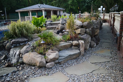 Kander K - Holmdel, NJ - A garden with a gazebo and a waterfall surrounded by rocks and pebbles