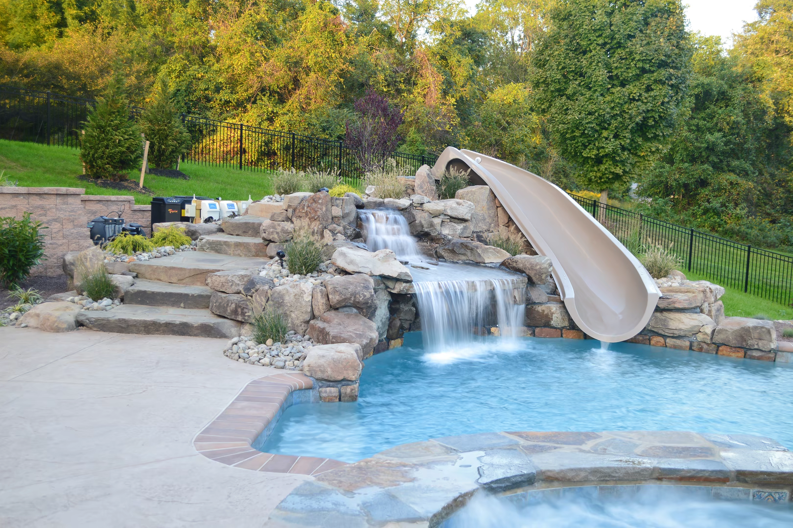 Natural stone boulder waterfall cascading into a pool surrounded by lush green foliage