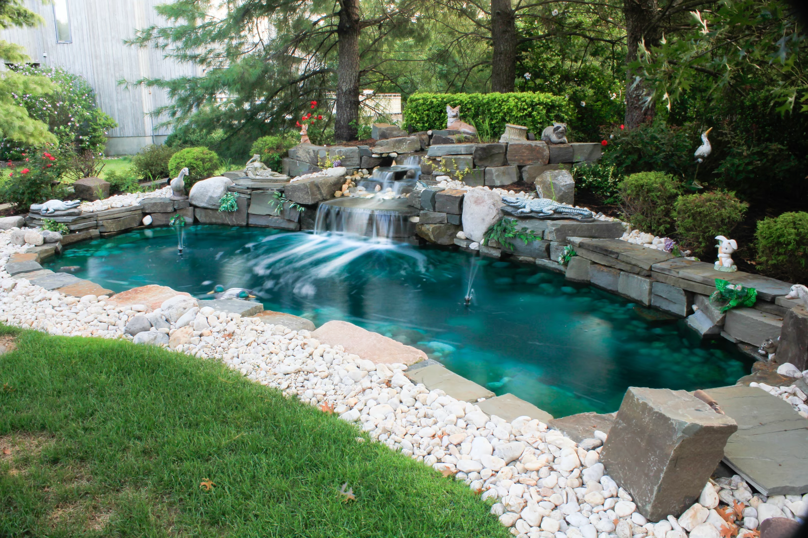 Natural stone boulder waterfall cascading into a pool surrounded by lush garden greenery