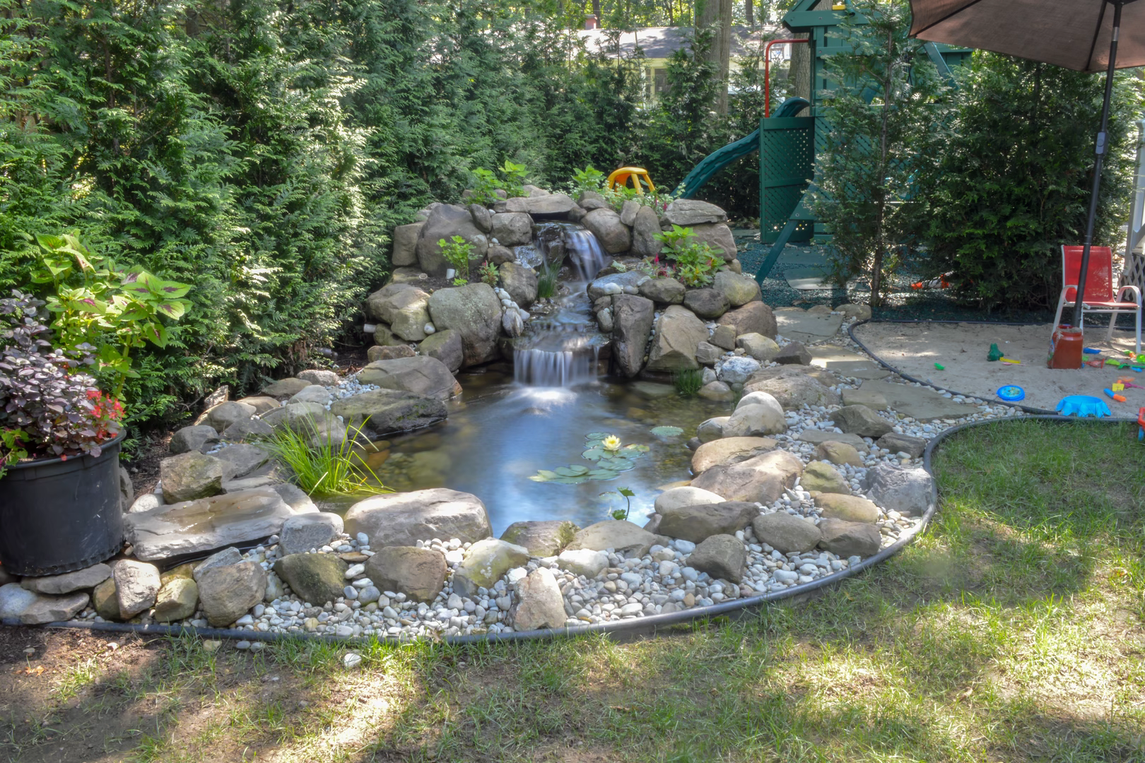 Natural stone boulder waterfall cascading into a garden pond surrounded by lush landscaping