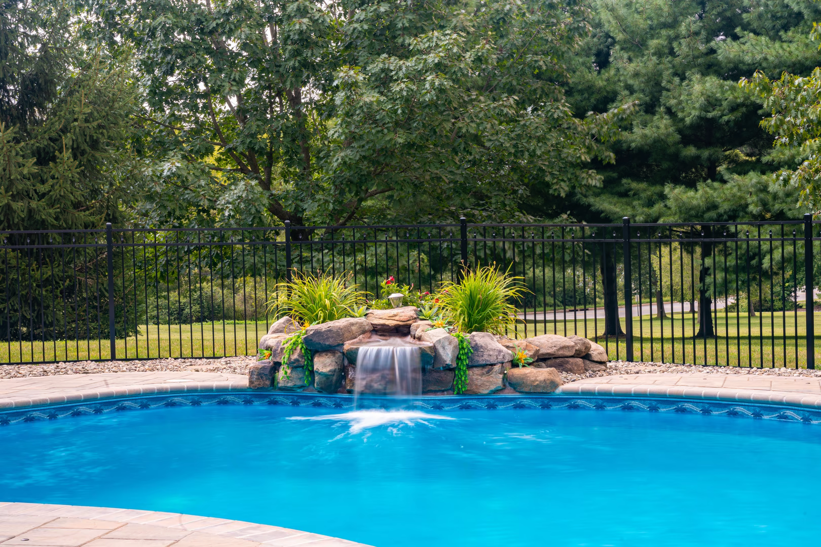 Natural stone boulder waterfall cascading into a pool framed by lush ornamental plants