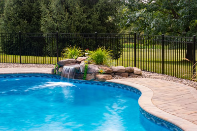 Lemolo D - Hackettstown, NJ - A blue swimming pool with a waterfall and landscaping around it
