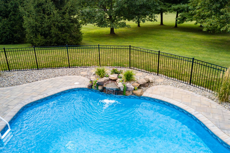 Natural stone boulder waterfall cascading into a blue pool with surrounding garden plants