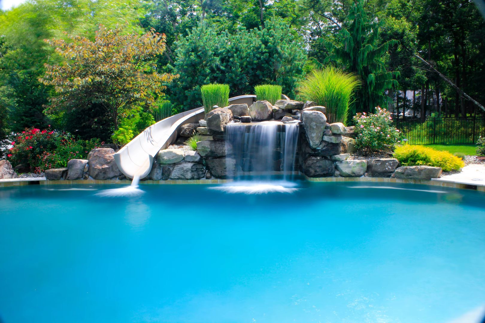 Natural stone boulder waterfall cascading into a pool bordered by lush garden plants