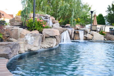 Lisbon F - Marlton, NJ - A backyard pool with a waterfall feature surrounded by rocks and flowers