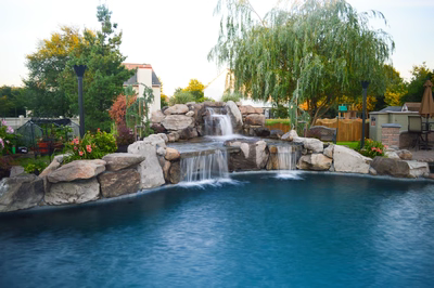 Lisbon G - Marlton, NJ - A backyard with a pool and waterfall feature surrounded by flowers and trees