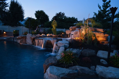 Lisbon L - Marlton, NJ - A backyard with a waterfall feature lit up at night, surrounded by rocks and plants