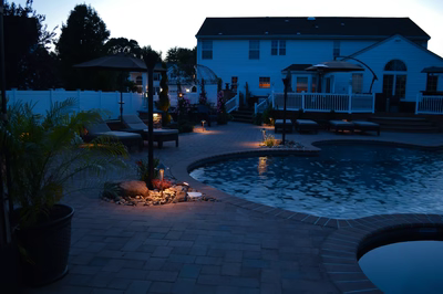 Lisbon N - Marlton, NJ - A backyard at night with a pool and patio area illuminated by lights