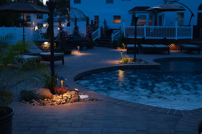 Lisbon O - Marlton, NJ - A backyard at night with a pool and patio area illuminated by lights