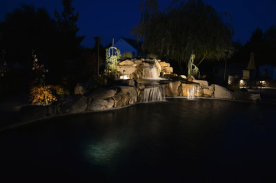 Lisbon R - Marlton, NJ - A pond with a waterfall lit up at night, surrounded by rocks and plants