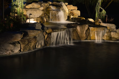 Lisbon V - Marlton, NJ - A water feature in a garden at night, surrounded by rocks and greenery