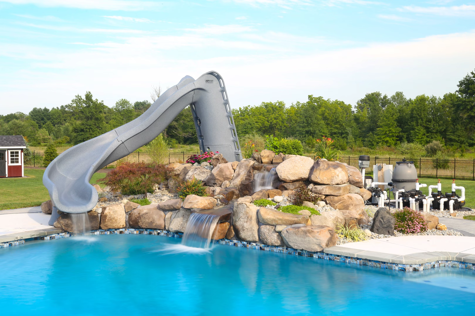 Natural stone boulder waterfall cascading into a pool with surrounding plants and slide