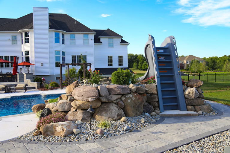 Natural stone boulder waterfall cascading into a swimming pool with surrounding garden plants