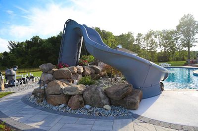 Loowit E - Ringoes, NJ - A large blue water slide sitting on top of a rock wall next to a swimming pool