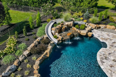 M Brown - Forrest Hills, MD - A swimming pool with a waterfall and a waterfall feature surrounded by lush greenery