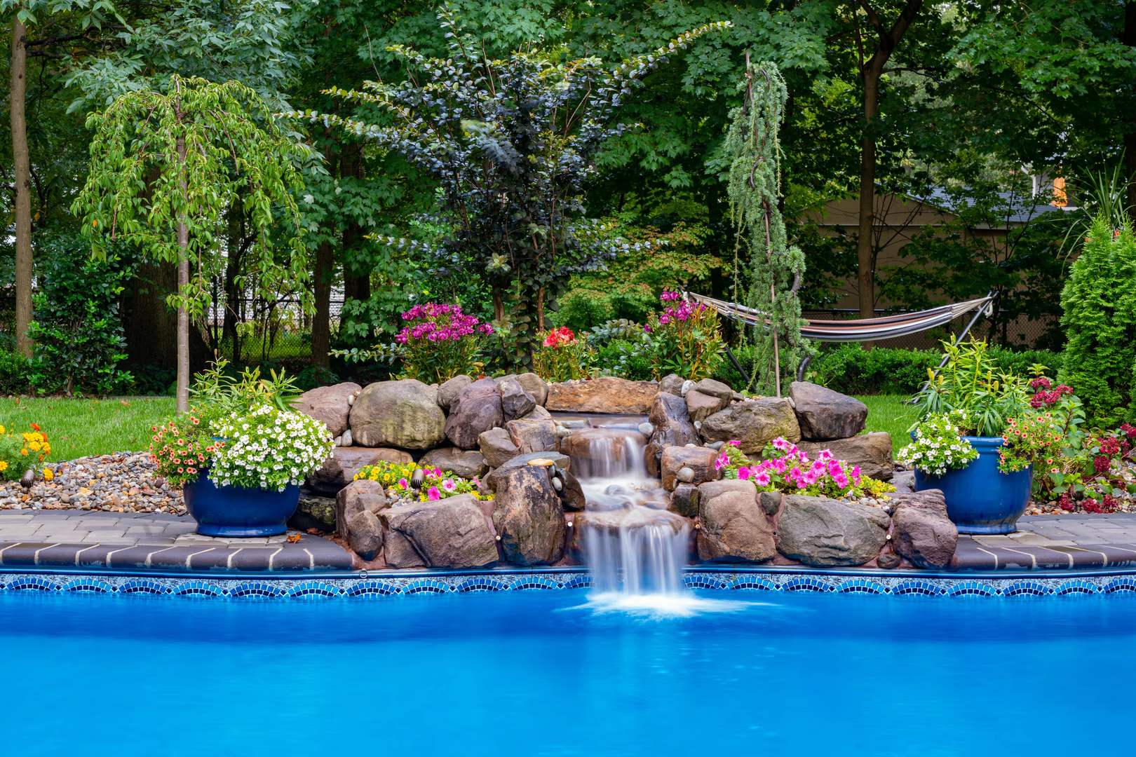 Natural stone boulder waterfall cascading into a pool surrounded by lush garden plants