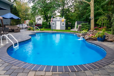 Manido G - Matawan, NJ - A blue swimming pool surrounded by a brick patio and landscaping.