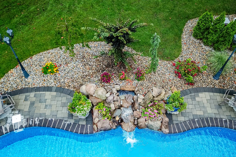 Natural stone boulder waterfall cascading into a pool surrounded by lush garden plants