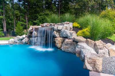 Masinga - Lumberton, NJ - A swimming pool with a waterfall in the middle surrounded by lush greenery