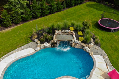 Masinga - Lumberton, NJ - A backyard with a swimming pool, a trampoline, and a waterfall