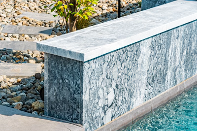 Memorial H - Cherry Hill, NJ - A close-up of a stone retaining wall next to a swimming pool with pebbles and a small tree in the background