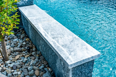 Memorial I - Cherry Hill, NJ - A concrete retaining wall next to a turquoise swimming pool with pebbles and a small tree