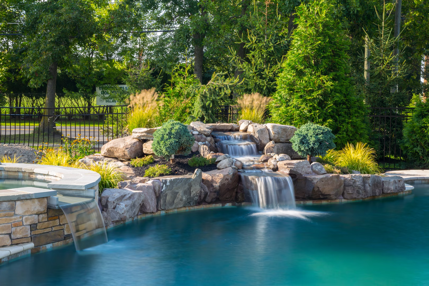 Natural stone boulder waterfall cascading into a pool surrounded by lush garden plants