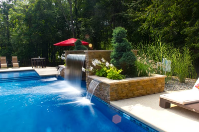 Middle C - Millstone, NJ - A swimming pool with a waterfall in the middle surrounded by lush greenery