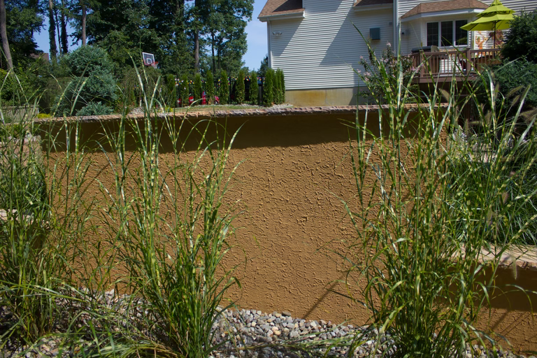 Natural stone boulder waterfall cascading into a backyard pool surrounded by zebra grass