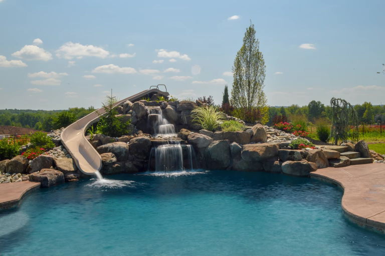 Natural stone boulder waterfall cascading into a pool with slide and lush landscaping