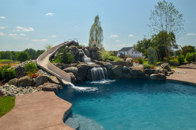 Miners B - Flemington, NJ - A swimming pool with a water feature and a slide surrounded by rocks and greenery