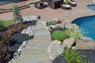 Miners I - Flemington, NJ - A backyard with a stone path leading to a swimming pool surrounded by rocks and plants