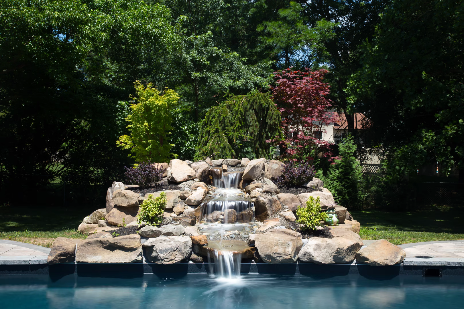 Natural stone boulder waterfall cascading into a pool surrounded by lush garden greenery