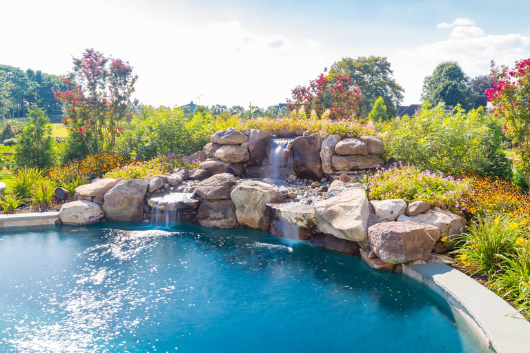 Natural stone waterfall cascading into a pool surrounded by lush, colorful garden plants