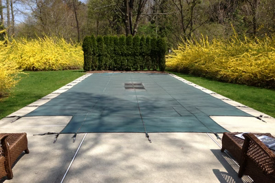 Morgan A - Saddle River, NJ - A concrete patio with a green tarp covering it, surrounded by lush green grass and yellow flowers
