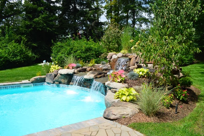 Morgan C - Saddle River, NJ - A backyard with a swimming pool surrounded by lush greenery and a waterfall