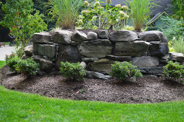 Natural stone boulder waterfall cascading into lush garden beds with ornamental grasses