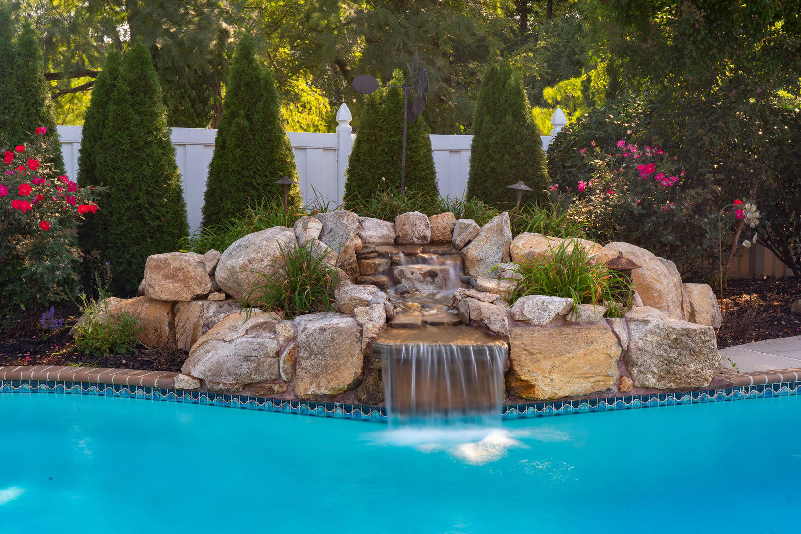Natural stone boulder waterfall cascading into a pool surrounded by lush garden greenery