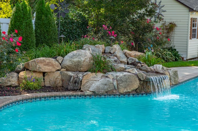 Multnomah D - West Deptford, NJ - A swimming pool with a waterfall in the middle surrounded by flowers and greenery